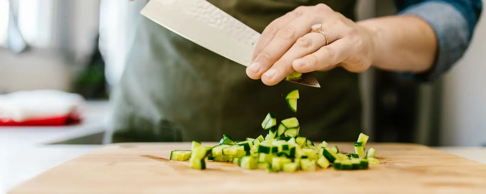 Hands dicing cucumber on a wooden chopping board in a home kitchen