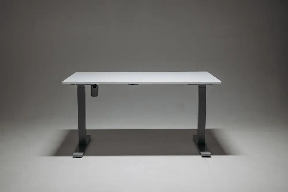Plain white height-adjustable desk on a two-leg frame in a studio