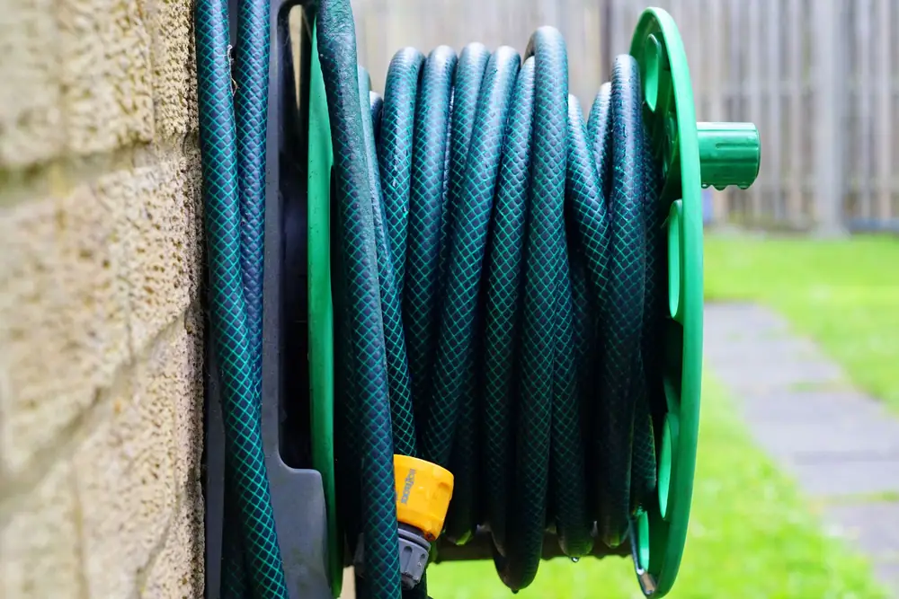 Garden hose coiled on a wall-mounted reel beside a brick wall
